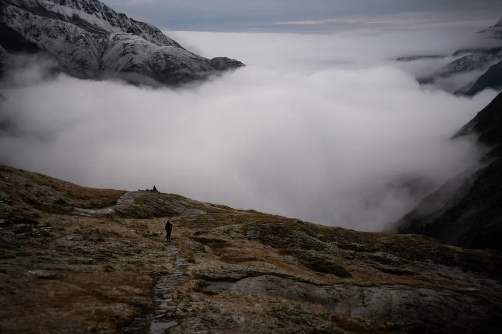A hiker follows a winding mountain path above a valley filled with clouds.
